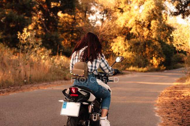Vista trasera de la mujer que monta la motocicleta en la carretera del campo en el bosque - foto de stock