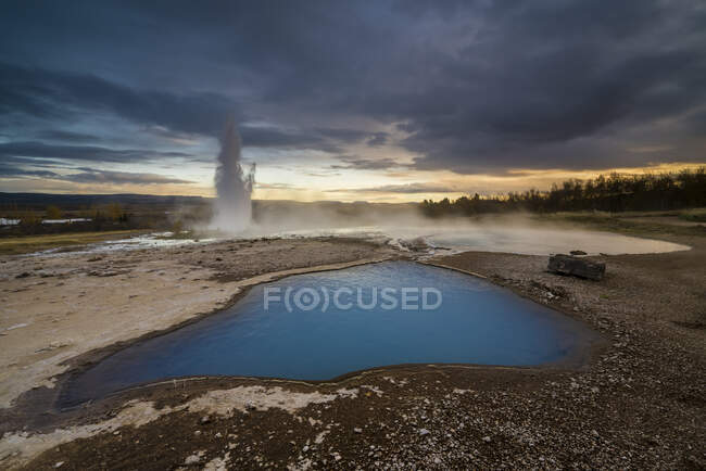Blue pond in geothermal area and geyser Strokkur erupting in the background, Geysir, Iceland — Stock Photo