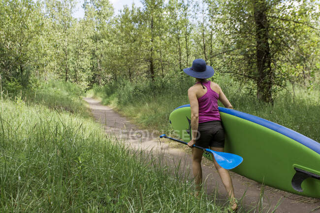 Una joven mujer lleva su tabla de remo a la playa en Oregon. - foto de stock