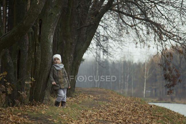 Маленькая девочка задумчиво стоит на берегу реки осенью. — стоковое фото