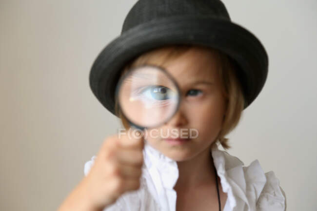 A girl in a hat looks through a magnifying glass. — Stock Photo