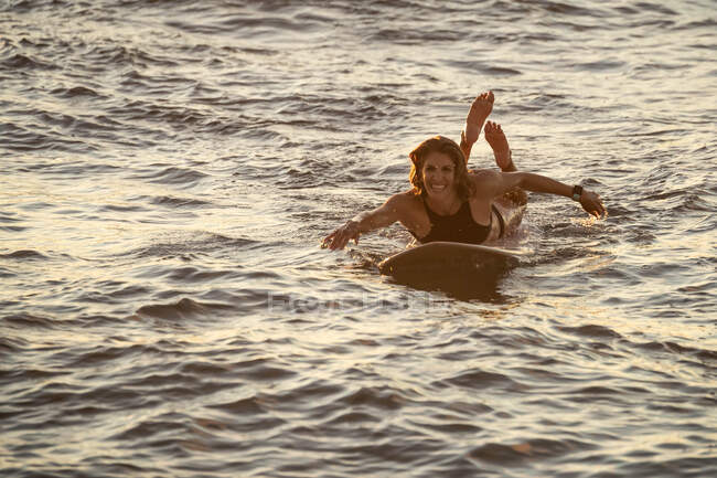 Paletas atléticas femeninas en tabla de surf al atardecer en Hawai - foto de stock