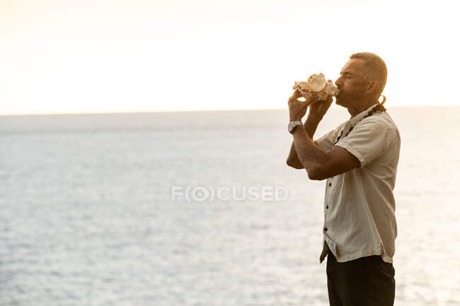 Male officiant blows conch shell in hawaii by the ocean — Stock Photo