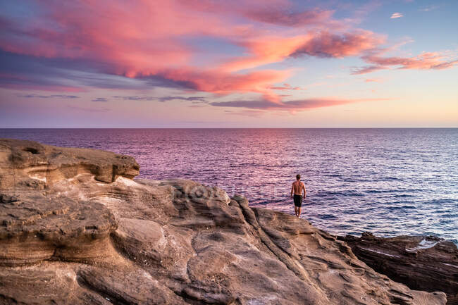 Adatto maschio si trova sul bordo della scogliera durante il tramonto hawaii rosa — Foto stock
