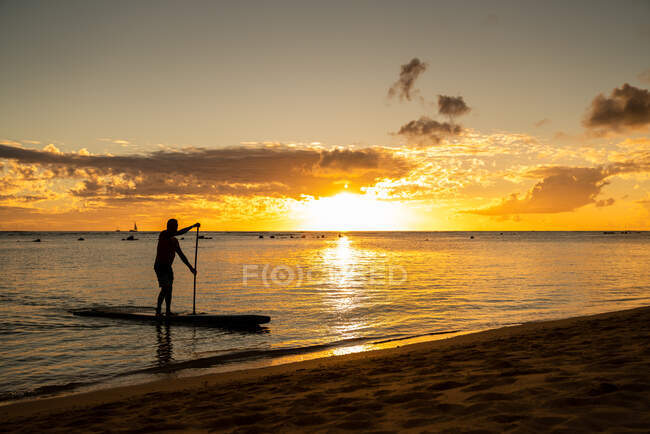 Мужчина встает весло посадки дрейфует на песок на закате — стоковое фото