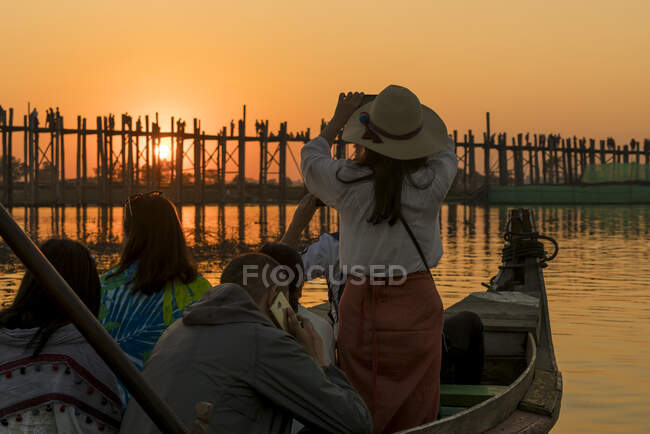 Turista feminina de pé no barco e fotografando ponte U Bein com telefone celular durante o pôr do sol, Amarapura, Mandalay, Myanmar — Fotografia de Stock
