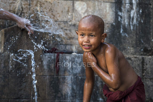 Novice shirtless monk bathing under running water outdoors, near Hsipaw, Myanmar — Stock Photo