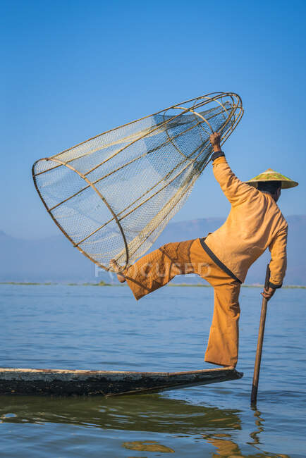 Rückansicht von Intha Fischer posiert mit typisch kegelförmigem Fischernetz auf einem Boot vor klarem blauen Himmel, Lake Inle, Nyaungshwe, Myanmar — Stockfoto