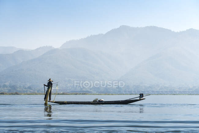 Fisherman using fishing net on boat against mountains, Lake Inle, Nyaungshwe, Myanmar — Stock Photo