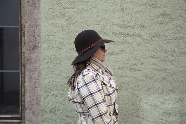 Donna che indossa un cappello e occhiali da sole in piedi da sola vicino a un muro di pietra — Foto stock
