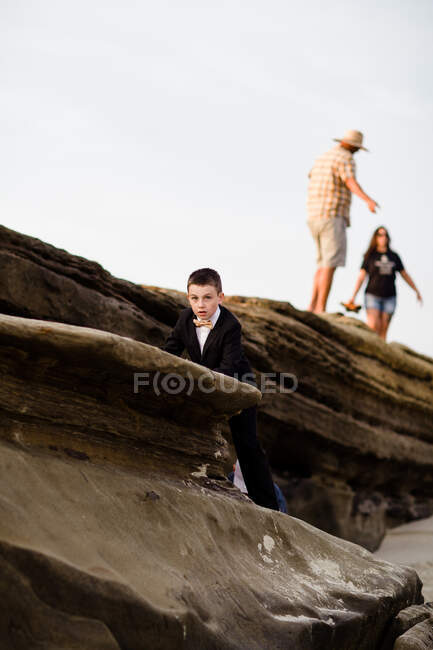 Niño de Nueve Años en Tux Escalando Rocas en la Playa en San Diego - foto de stock