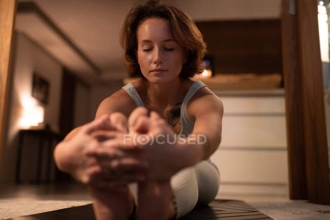 Femme aux yeux fermés posant Pascimottanasana pendant un cours de yoga à la maison — Photo de stock