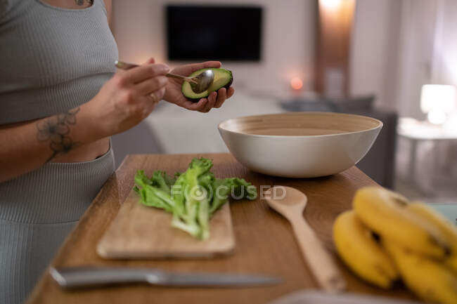Mulher anônima removendo sementes de abacate enquanto cozinha salada saudável em casa — Fotografia de Stock