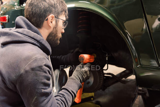 Photo of a young man in a garage performing repairs on old car — Stock Photo