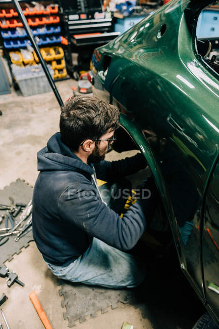 Foto de un joven en un garaje realizando reparaciones en un coche viejo - foto de stock