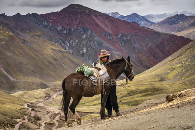 Horseman standing by horse on Rainbow Mountain trail with high Andes mountain in background, Pitumarca, Peru — Stock Photo