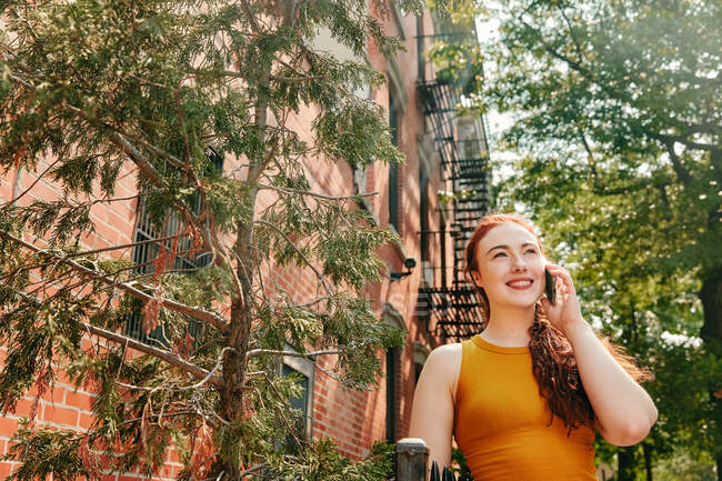 Mujer joven felizmente hablando por teléfono al aire libre en la calle Brooklyn - foto de stock