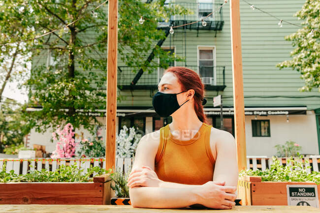 Young woman sitting in an outdoor restaurant table, wearing facemask — Stock Photo