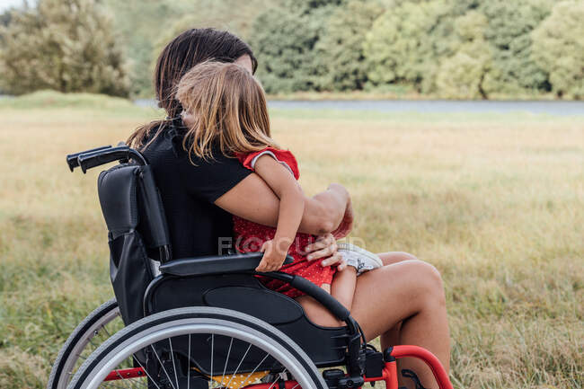 Disabled mother in a wheelchair hugging her little daughter with a gre — Stock Photo