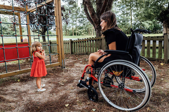 Маленькая девочка играет в парке со своей матерью в инвалидном кресле — стоковое фото