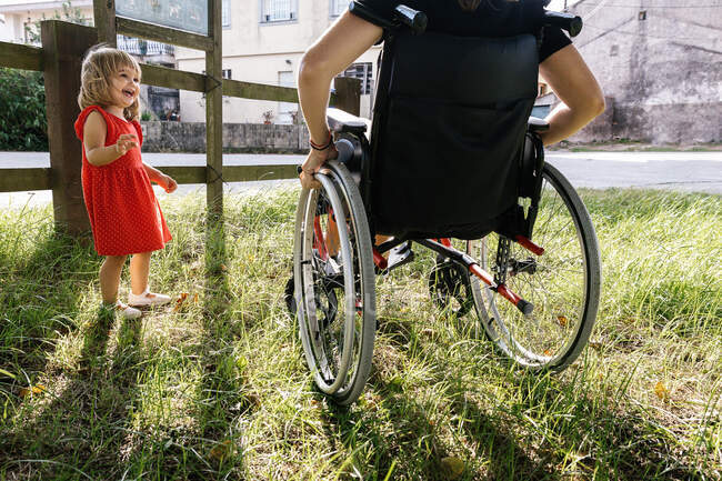 Menina sorrindo ao lado de sua mãe em uma cadeira de rodas em um fiel verde — Fotografia de Stock