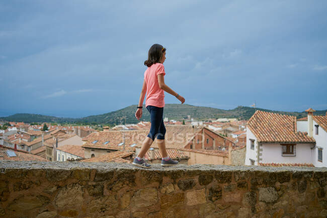 Menina vestindo uma blusa rosa andando em uma parede de pedra com ho — Fotografia de Stock