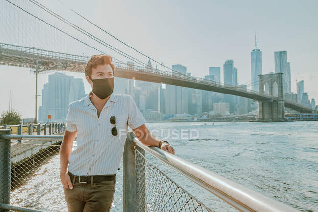 Молодой человек стоит у реки в маске для лица — стоковое фото