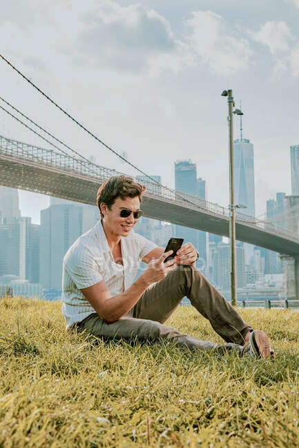 Молодой человек сидит на улице в парке по телефону — стоковое фото