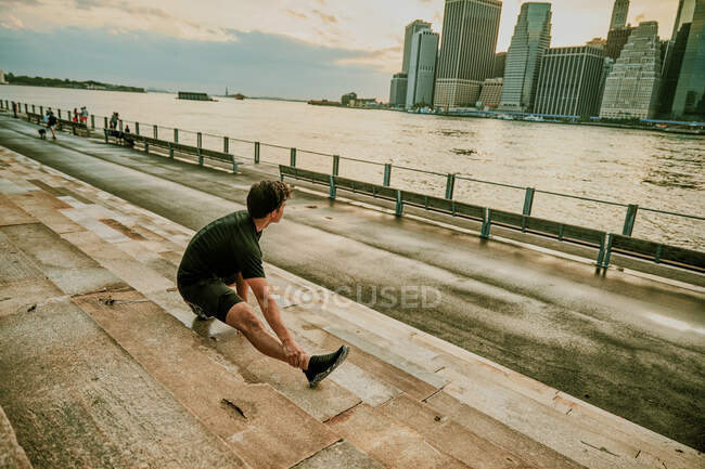 Atleta masculino estirándose en el paseo marítimo durante el atardecer - foto de stock