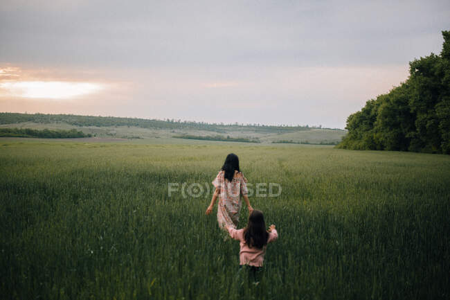 Madre e hija caminando en el campo al atardecer - foto de stock