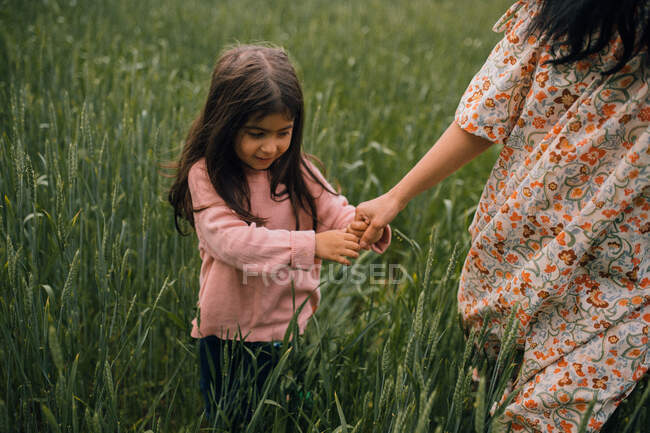 Улыбающаяся девушка держит маму за руку во время прогулки по полю — стоковое фото