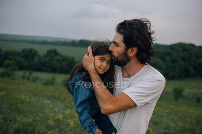 Father carrying and kissing daughter outdoors in field — Stock Photo
