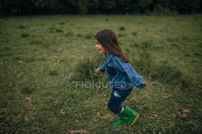 Menina rindo correndo através do campo em botas de chuva — Fotografia de Stock