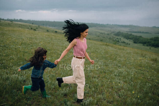 Mamá y su hija corriendo colina abajo en el campo - foto de stock