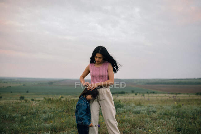 Mãe fixação filhas cabelo ao entardecer ao ar livre — Fotografia de Stock