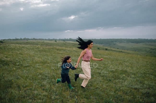 Мама і дочка біжать на пагорбі в сільській місцевості — стокове фото