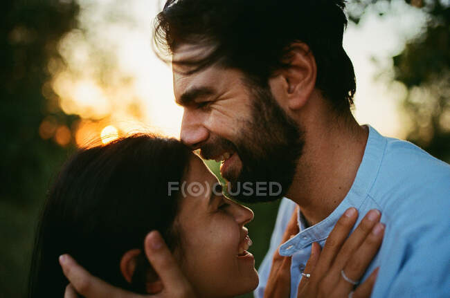 Мужчина смеется, целуя жену на улице на закате — стоковое фото