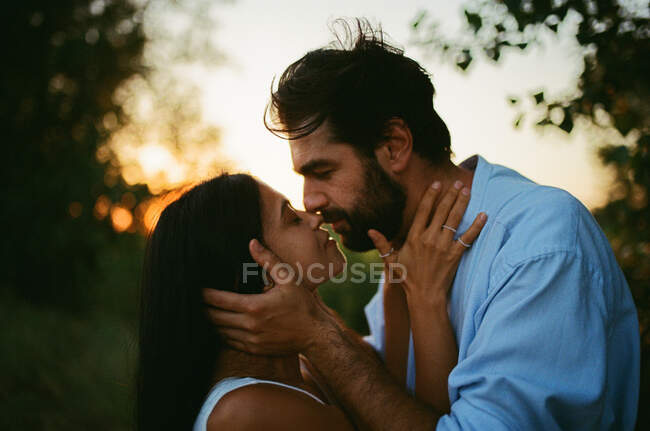 Hombre y mujer besándose al aire libre al atardecer - foto de stock