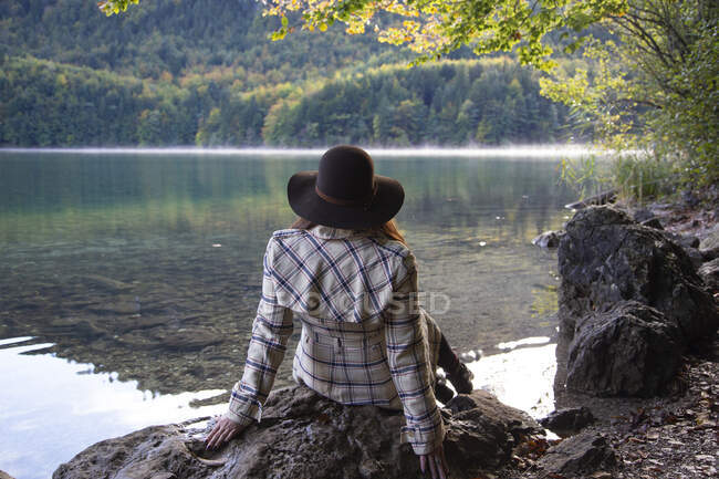Una persona sentada y relajada junto a un lago alpino - foto de stock
