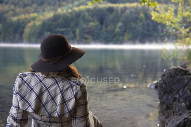 A woman wearing a hat sits by a crystal clear lake in Germany — Stock Photo