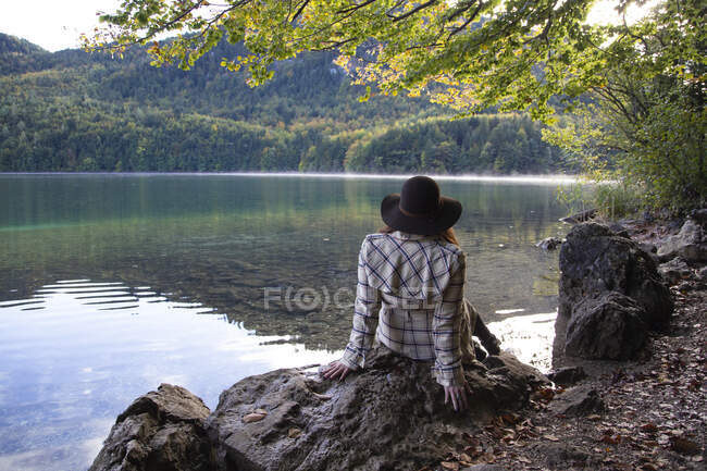 Eine Frau sitzt gemütlich unter einem Baum am Alpensee — Stockfoto