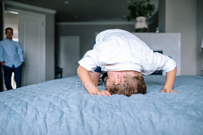 Мальчик играет на кровати родителей, пока папа смотрит — стоковое фото