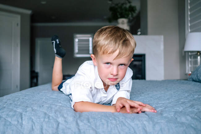 Bambino in età prescolare con faccia arrabbiata posa su un grande letto — Foto stock