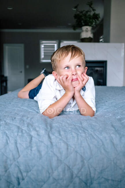 Молодий хлопчик лежить на великому ліжку, дивлячись на щось — стокове фото