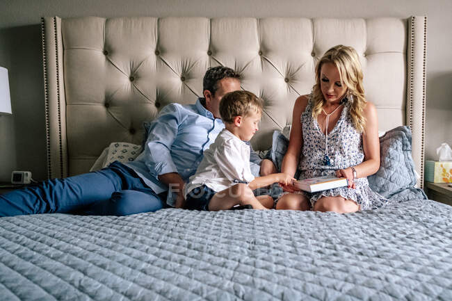 Retrato horizontal de una familia sentada en una cama leyendo un libro - foto de stock