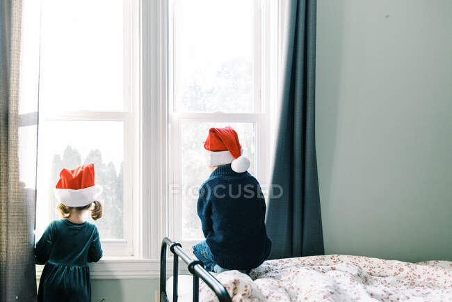 Deux enfants regardant par la fenêtre attendant le Père Noël — Photo de stock