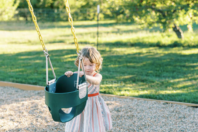 Petite fille voulant se balancer dans la balançoire de bébé à une aire de jeux — Photo de stock