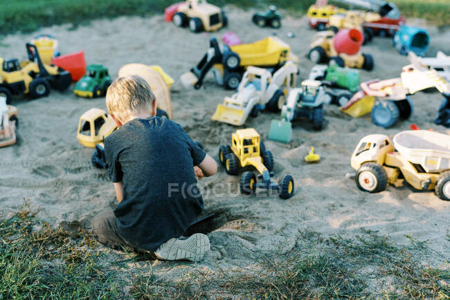 Ragazzino che gioca con una serie di camion giocattolo — Foto stock