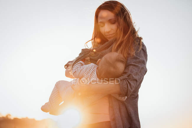 Mom smiling breastfeeding baby outdoors during sunset — Stock Photo