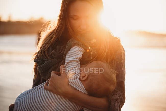 Close up da mãe amamentando bebê na praia durante o pôr do sol — Fotografia de Stock